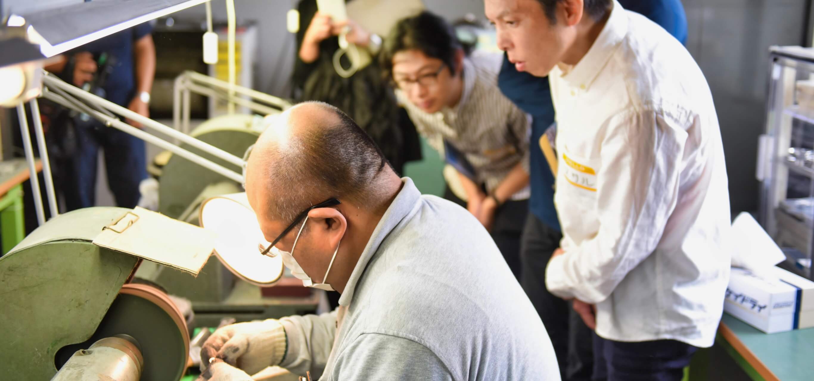 写真：松一の代表取締役・松澤さんが研磨機を扱う様子を眺める見学者の様子